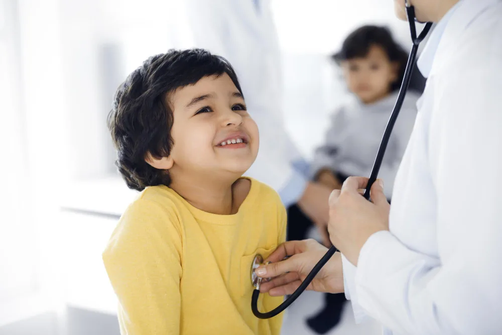 A doctor examining a smiling young child with a stethoscope during a paediatric consultation